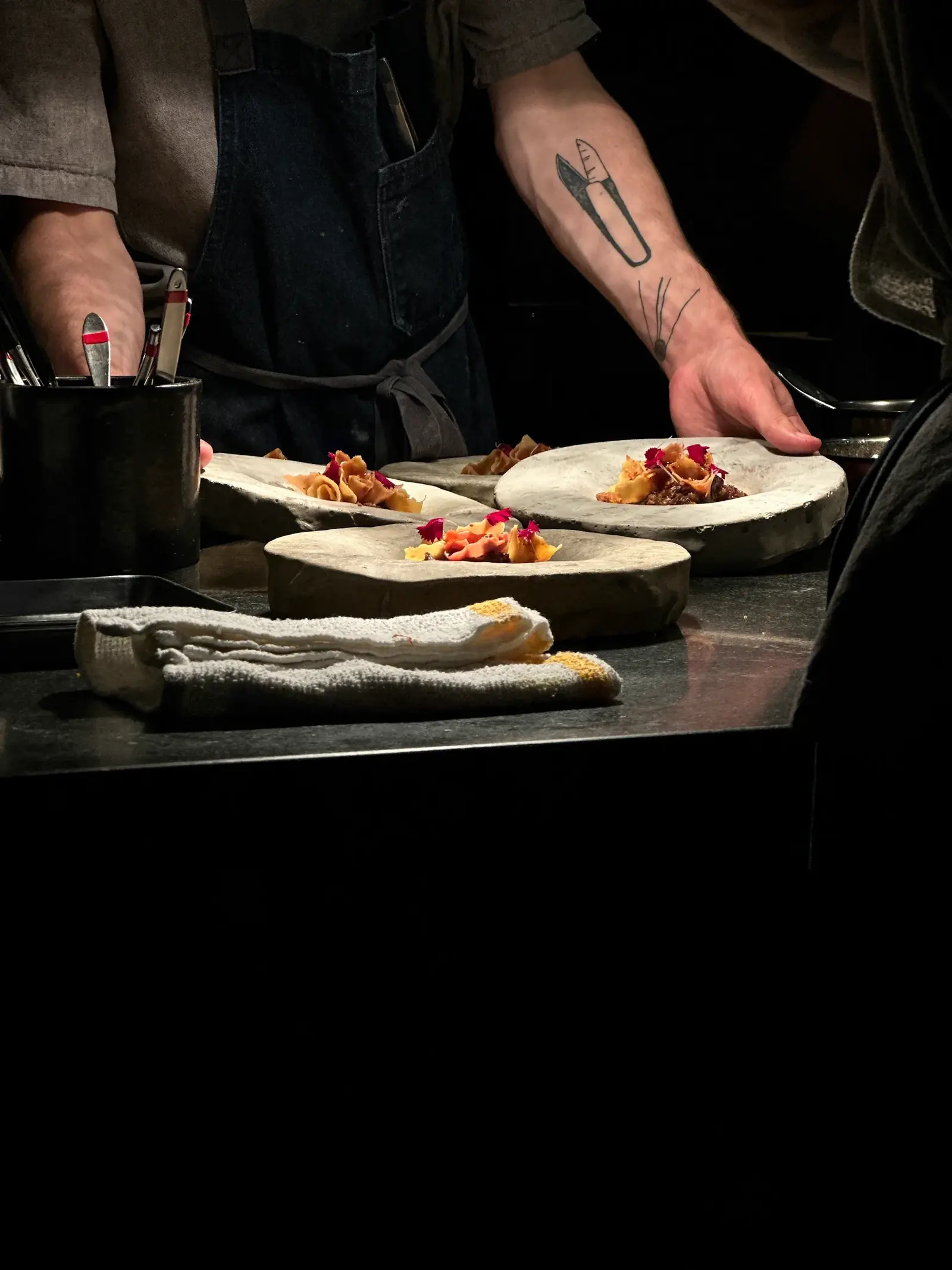 A cook in a dark kitchen plating filled pasta onto three stone bowls at the pass.